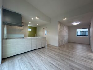 滋賀の平屋LDK別角度｜白いキッチンとグリーンアクセントウォールの明るいリビングダイニング｜つなぐハウス