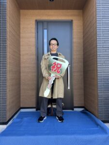 滋賀県で完成した平屋の注文住宅。木目調の玄関ドアの前で大きな鍵を持つお引渡し式の施主様。