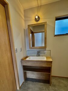 滋賀県で個性的な平屋の注文住宅を手がける「つなぐハウス」の施工例。玄関横の壁にOSB合板を採用し、無骨ながらも温かみのあるガレージライクな雰囲気を演出。上下に配置した窓が空間に抜け感を与えます。滋賀でデザイン性の高い平屋や、趣味を楽しむ家づくりをご検討中の方に人気のデザインです。